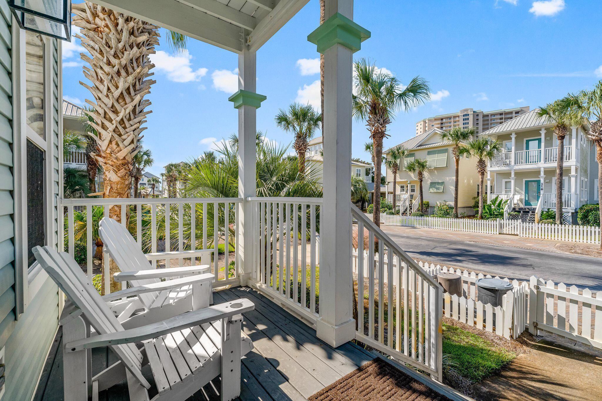 A wooden porch with white railings and two Adirondack chairs.