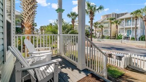 A wooden porch with white railings and two Adirondack chairs.