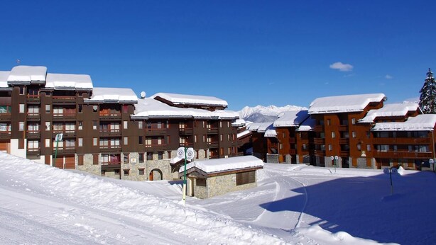 A snow-covered building with multiple balconies and a ski slope in the foreground.