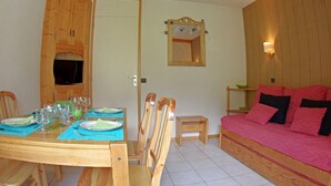 A dining area with a wooden table set for four, a wooden cabinet with a television, and a red sofa.