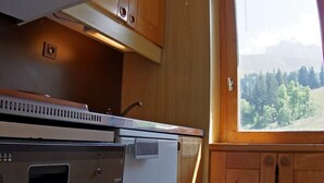 A compact kitchen with a microwave, stove, and sink, wooden cabinets, and a window with a mountain view.