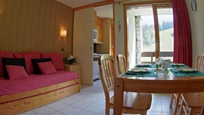 A cozy room with a wooden sofa, a dining table set for four, and a kitchen in the background.