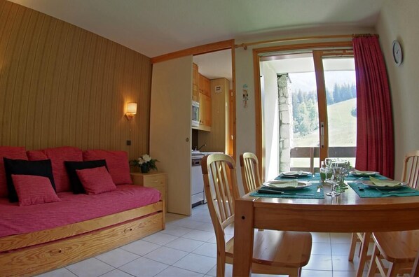 A cozy room with a wooden sofa, a dining table set for four, and a kitchen in the background. - 1st floor, view ski slopes, balcony, tv, 25m², Valmorel (Valmorel)