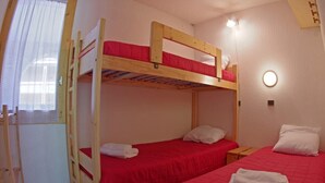 A room with two bunk beds, each with a red bedspread and white pillows. There is a small wooden nightstand with a lamp on it.