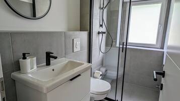 Ein modernes Badezimmer mit einem weißen Waschtisch, einem runden Spiegel, einer Toilette und einer Duschkabine.