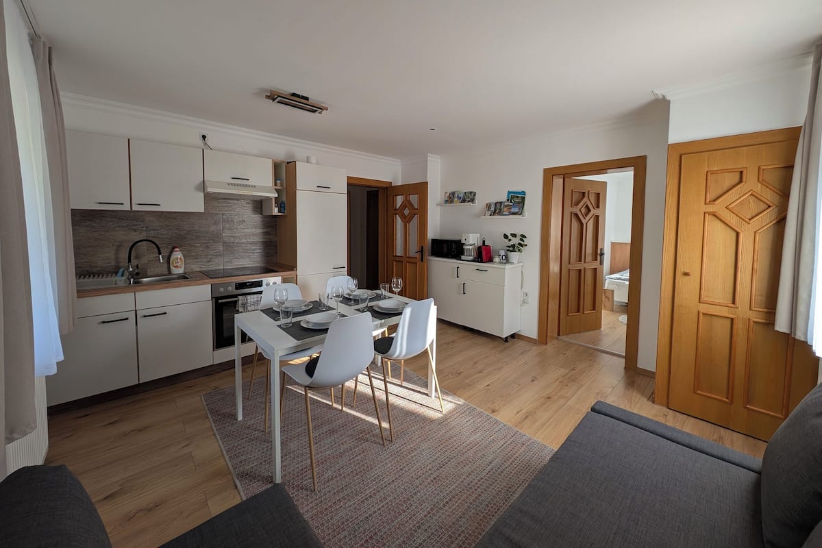 A modern kitchen with white cabinets, a dining table set for four, and a coffee machine.
