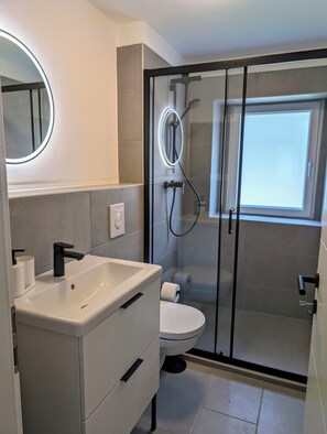 A modern bathroom with a white sink, toilet, and glass-enclosed shower.