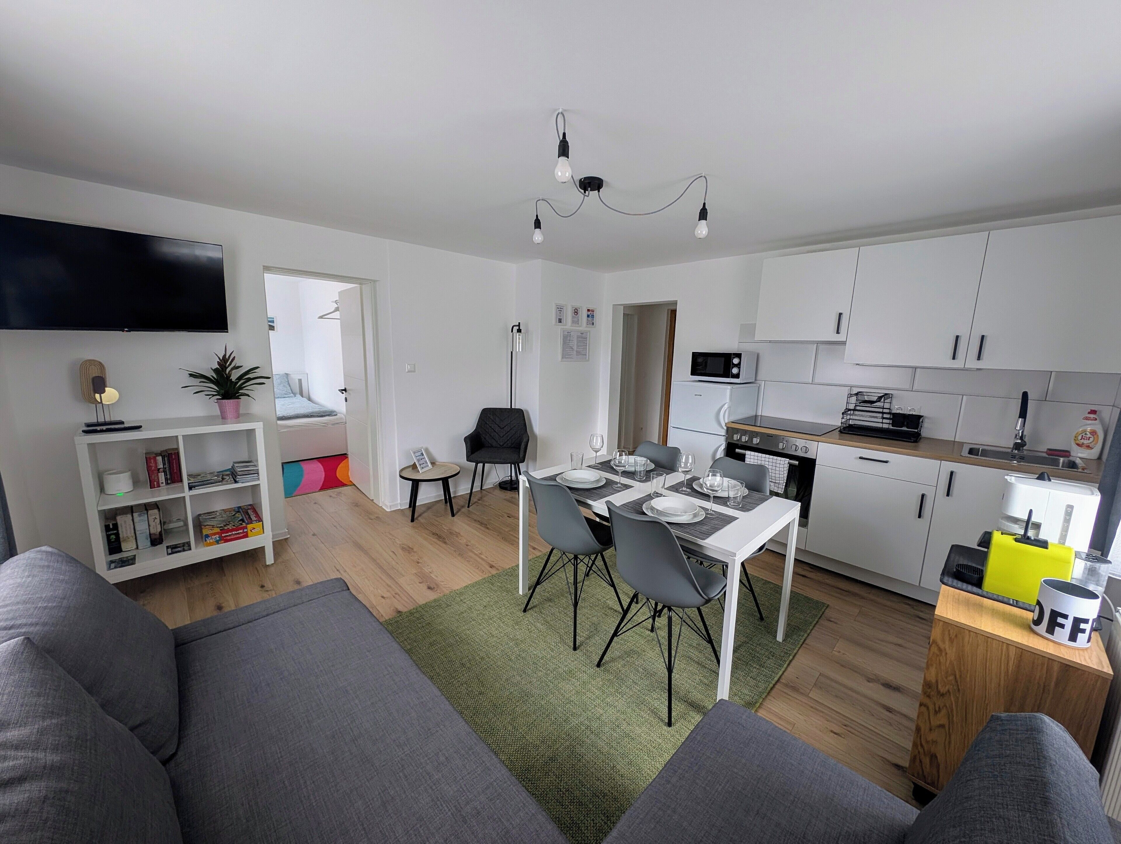 Een modern appartement met een eethoek, keuken, woonkamer en een tv aan de muur.