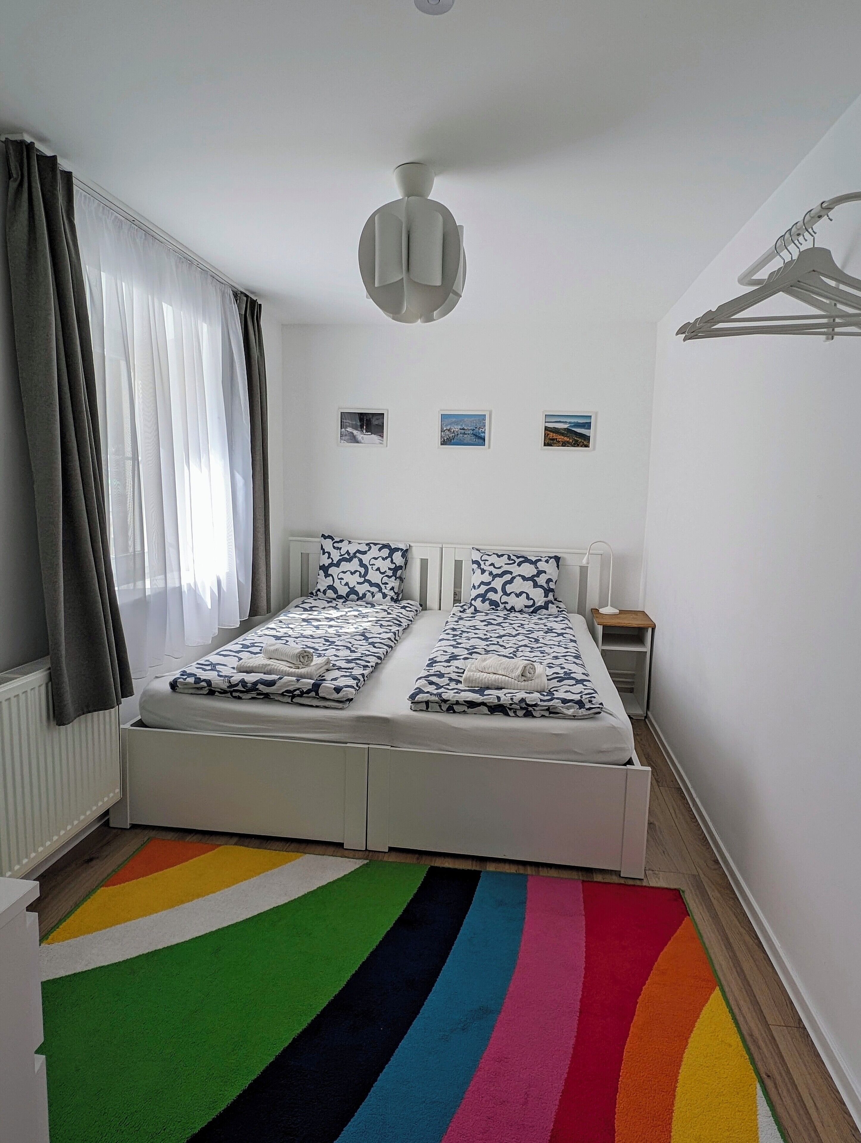 Ein Schlafzimmer mit Bett, Nachttisch, Lampe und farbenfrohem Teppich.