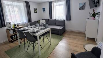 Una sala de estar moderna con comedor, sofá, televisión y una planta pequeña.