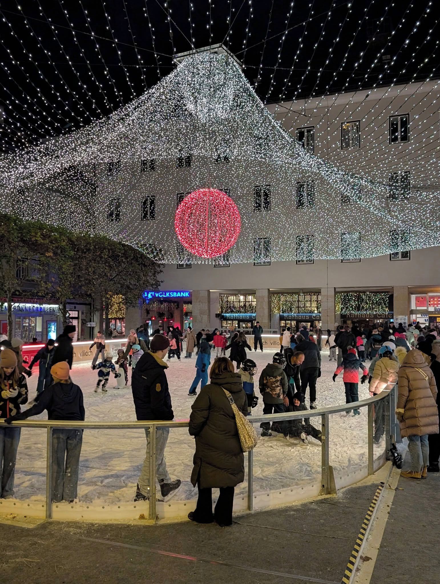 An indoor ice rink with people skating and spectators watching.