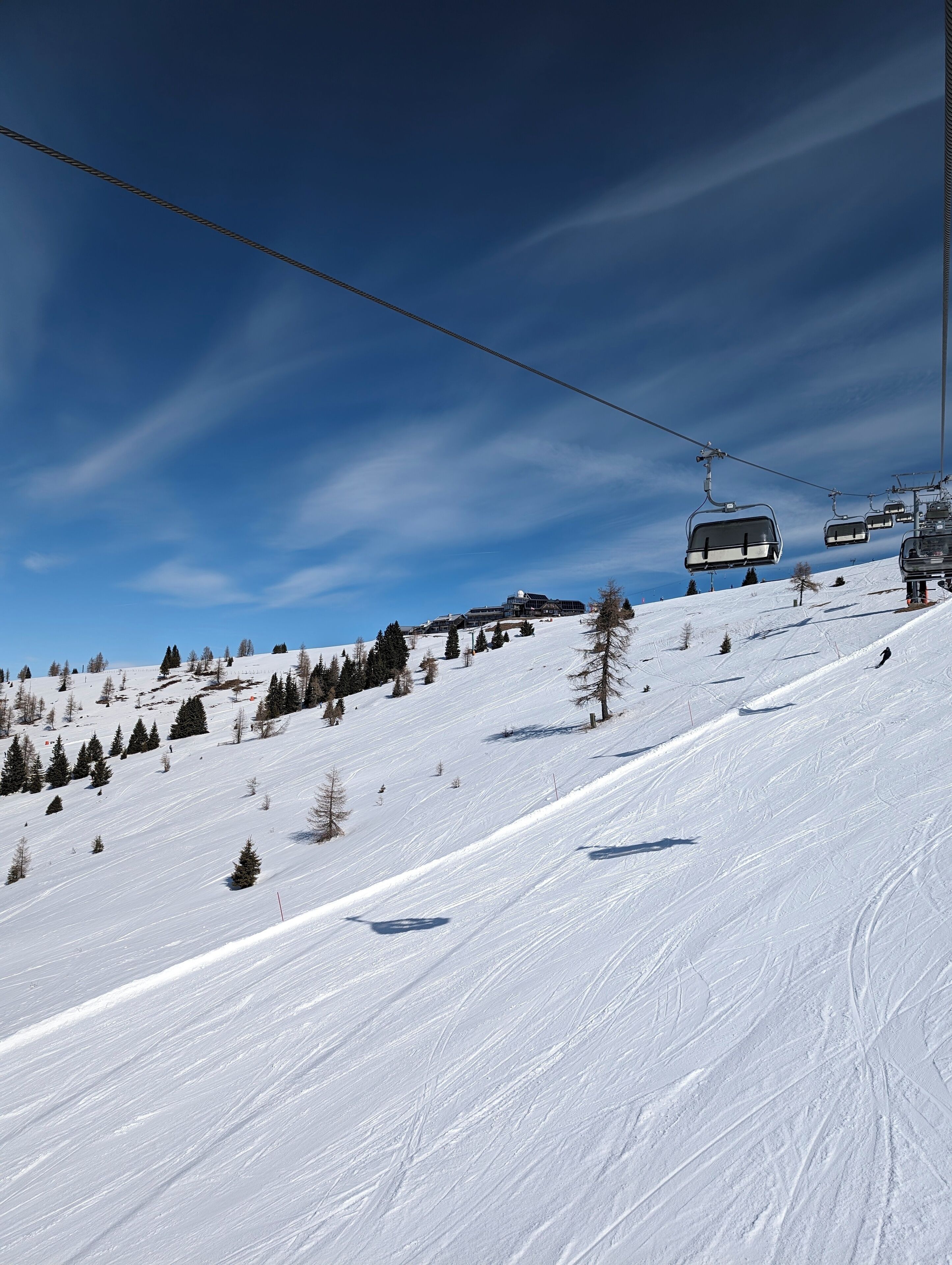 Eine Seilbahn auf einem verschneiten Hang bei blauem Himmel.