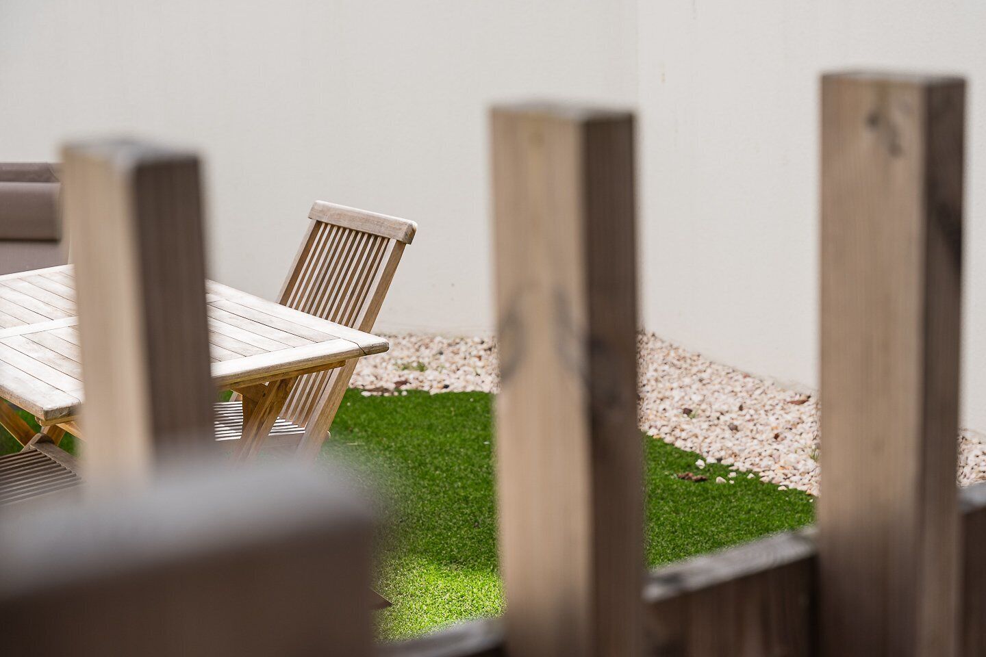 Une table et des chaises en bois sont disposées à l’extérieur, avec un mur blanc en arrière-plan.