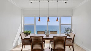 Comedor con vista al océano, que incluye una mesa con seis sillas, luces colgantes y plantas en macetas.
