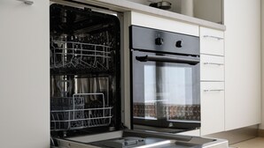 An open dishwasher and an oven in a modern kitchen with white cabinets.