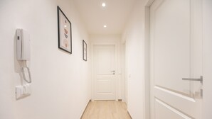 A hallway with a white door at the end, a phone on the wall, and framed pictures on the wall.