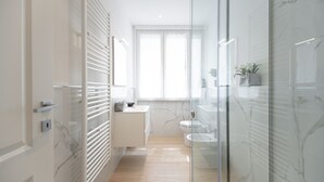 A modern bathroom with a glass shower enclosure, a marble-tiled wall, and a wooden floor.