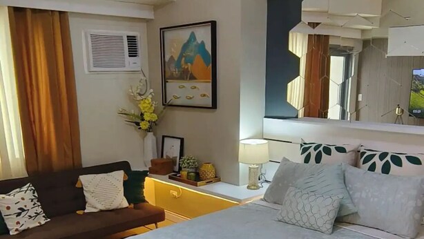 Una habitación de hotel con una cama grande, un sofá, una mesita de noche y una lámpara en el techo.