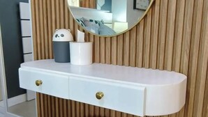 Un tocador con un espejo redondo, una mesa consola blanca y un taburete dorado frente a una pared de madera.
