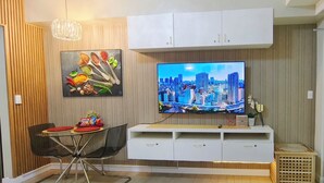 Una sala de estar moderna con un televisor de pantalla plana, una zona de comedor con mesa y sillas, y un mueble blanco para entretenimiento.