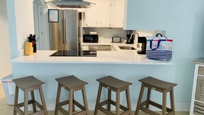 Une cuisine moderne dotée d’un îlot central, d’appareils électroménagers en acier inoxydable et de trois tabourets en bois.