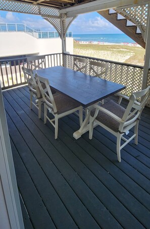 Ein überdachter Außenbereich mit Tisch und Stühlen mit Blick auf einen Strand.