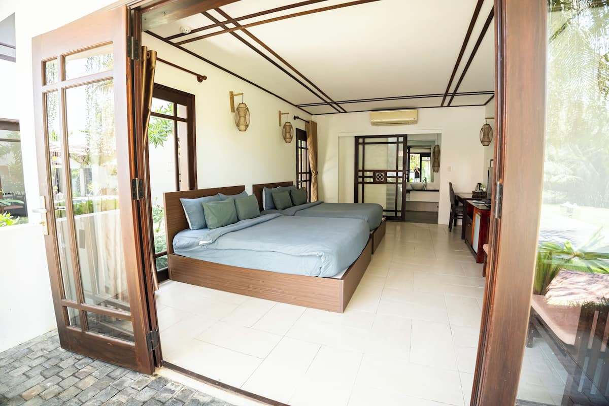 A bedroom with a large bed, a dining area, and a view of greenery outside.