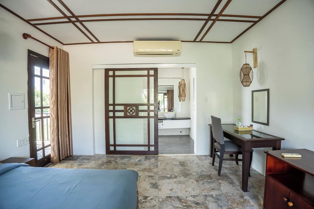 A hotel room with a bed, a desk, a chair, and a bathroom visible through an open door.