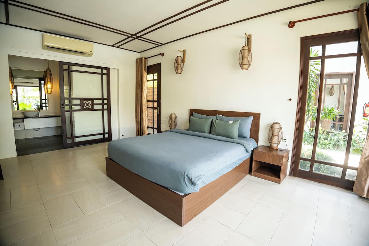 A modern bedroom with a large bed, a wooden nightstand, and a view of the garden through a sliding door.
