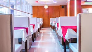 Una hilera de mesas blancas con manteles rojos en un comedor con paneles de madera y una araña.