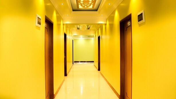Un pasillo de hotel con paredes amarillas y puertas, suelo pulido y techo decorativo.