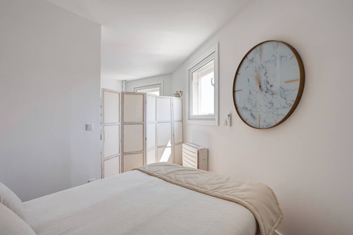 Un dormitorio con cama, armario, radiador y un reloj de pared.