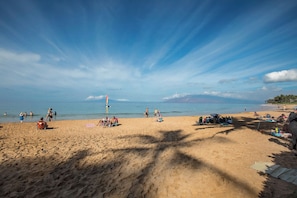Una playa con gente tomando el sol y nadando, una torre de salvavidas y un cielo despejado.