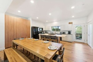 A modern kitchen with white cabinets, a wooden dining table, and a built-in island.