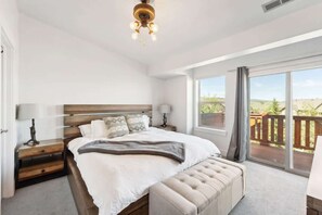 Ein Schlafzimmer mit einem großen Bett, einem Nachttisch, einer Bank und Blick ins Freie durch eine Schiebetür.