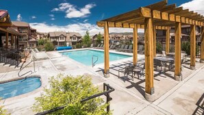 Area piscina con un gazebo in legno, sedie a sdraio e vista su edifici residenziali.
