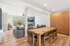 A modern living room with a wooden dining table, grey sofa, and a fireplace.