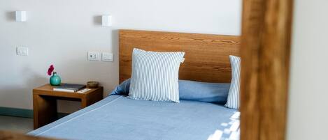 A neatly made bed with a wooden headboard, a small bedside table with a vase and a bowl, and a wall socket.