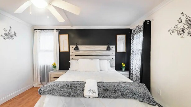 Un dormitorio con una cama, una mesita de noche, un ventilador de techo y decoración en las paredes.