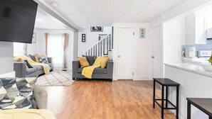 Una sala moderna con un sofá gris, un televisor negro y una escalera que lleva a otra habitación.