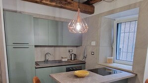 A modern kitchen with a central island, bar stools, a hanging light fixture, and a window with bars. - Vicolo d'Este (Tivoli)
