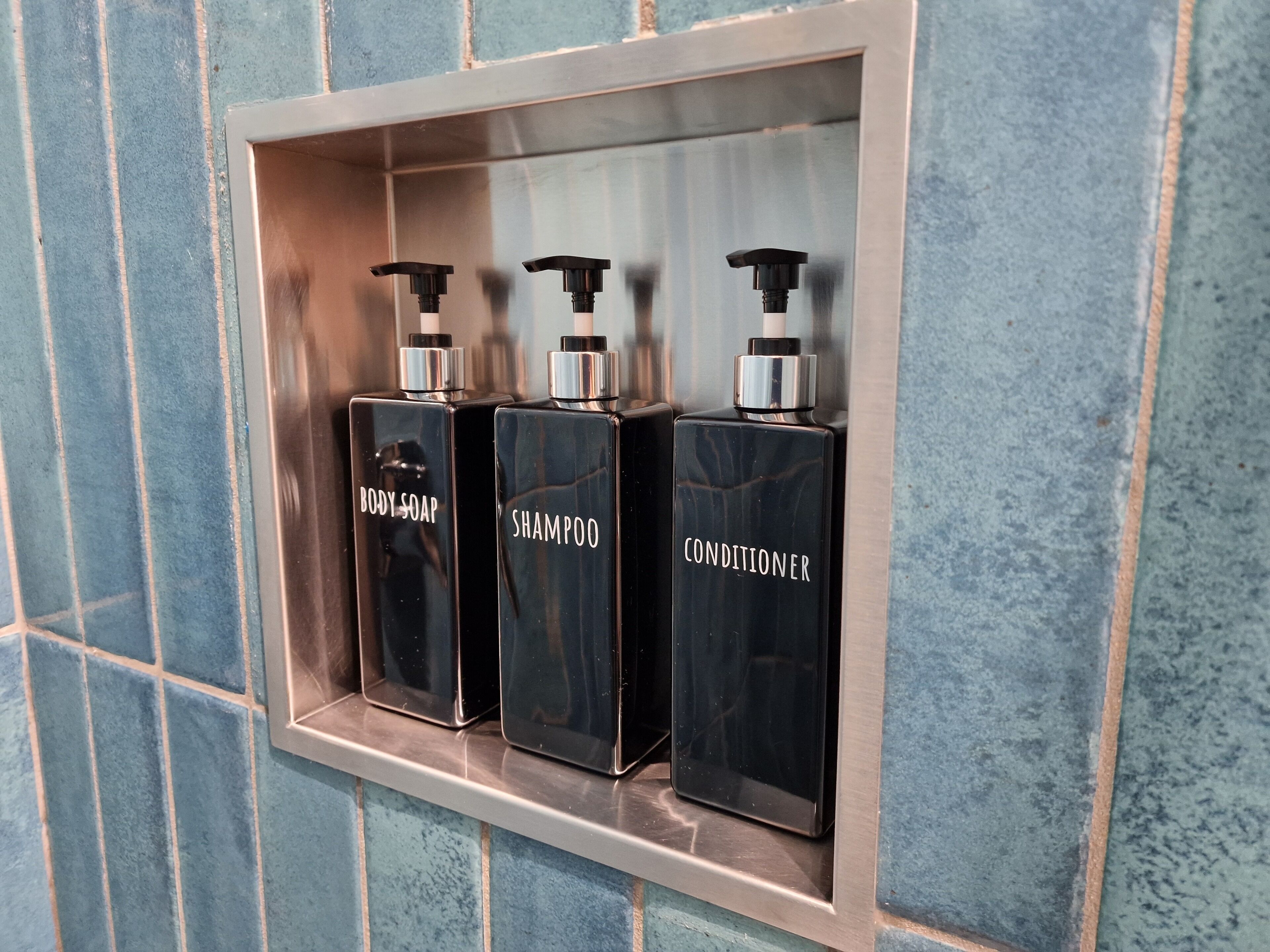 A shelf with three black bottles labeled body soap, shampoo, and conditioner.