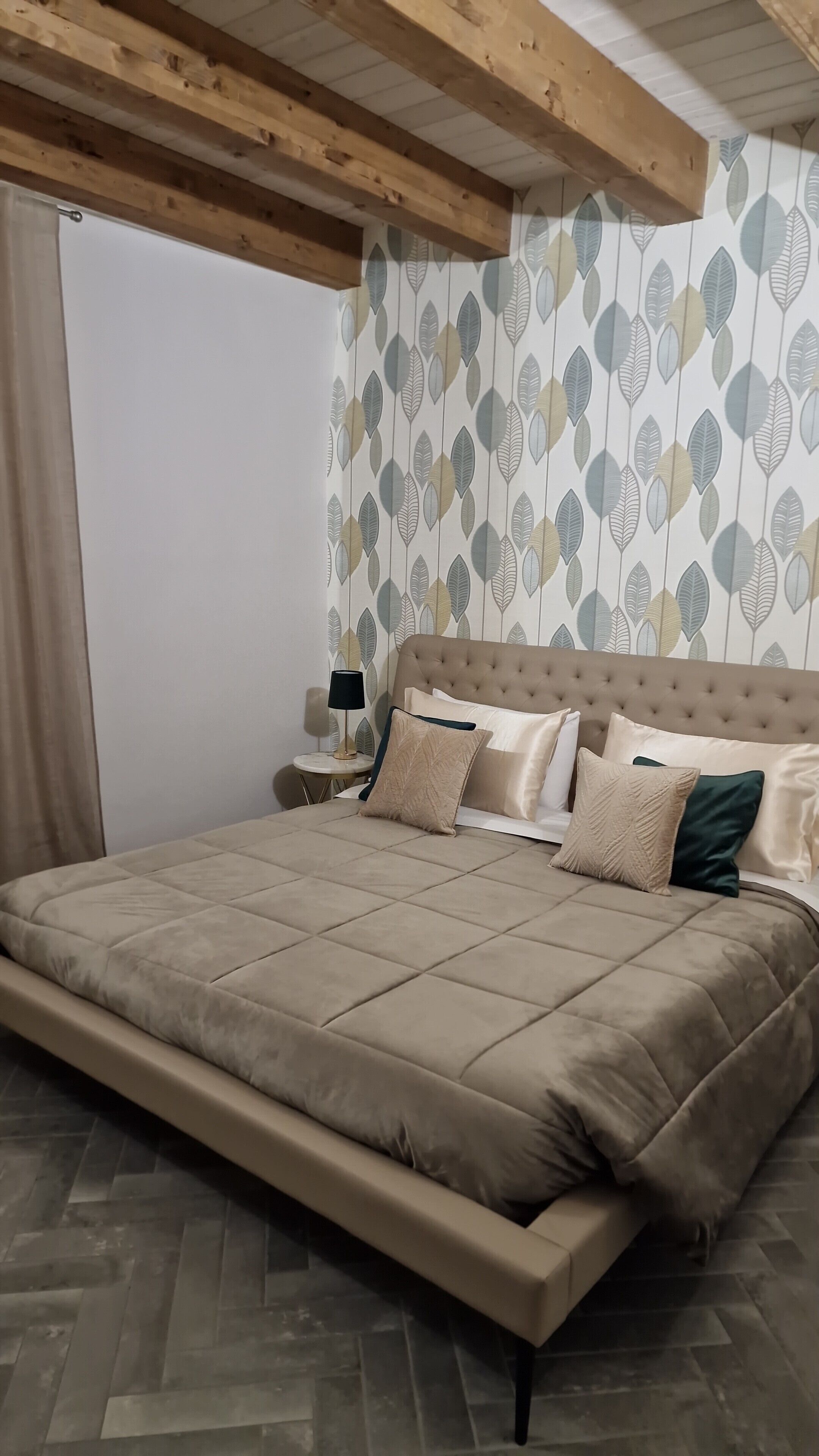 Quarto com uma cama grande, mesa de cabeceira, abajur e papel de parede estampado.
