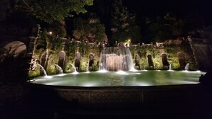 A nighttime view of a water feature with multiple cascades, surrounded by stone structures and greenery. - Vicolo d'Este (Tivoli)