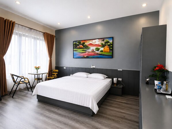 Ein modernes Hotelzimmer mit einem großen Bett, einem kleinen Tisch mit Stühlen, einem Bild an der Wand und Blick ins Freie.