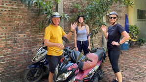 Three people standing in front of a brick wall with a motorcycle parked nearby. - Tam Coc Phuong Nhi Homestay (Nam Hoa Lu)