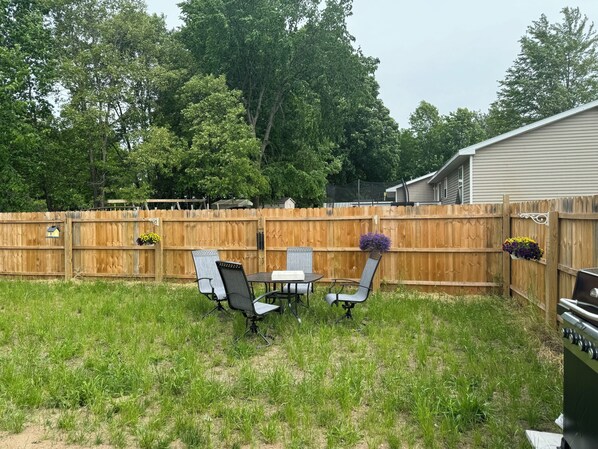 A backyard with a wooden fence, a grill, and two chairs with a table.