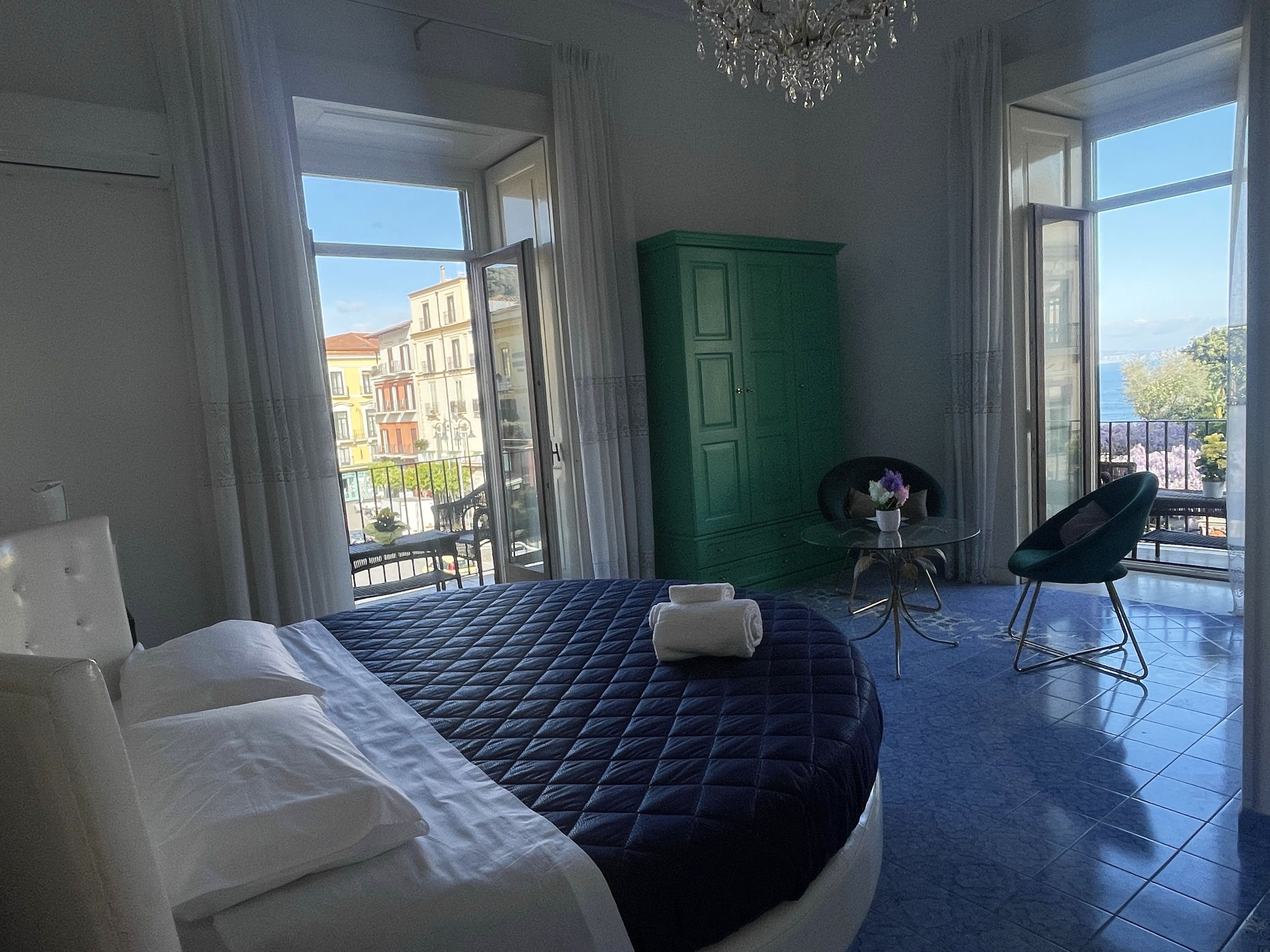 A bedroom with a large bed, a green wardrobe, a small table with a vase, and a chair.