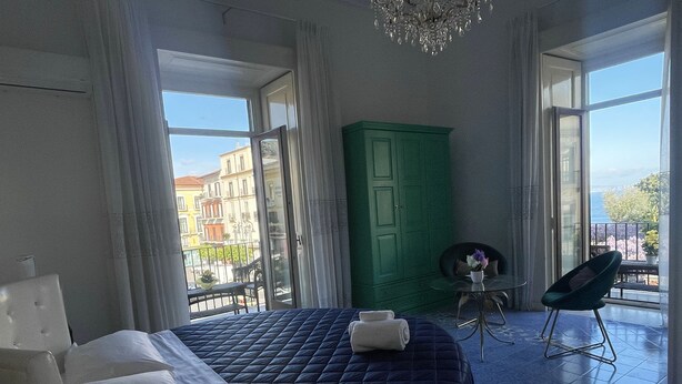 Een slaapkamer met een groot bed, een groene garderobe, een klein tafeltje met een vaas en een stoel.