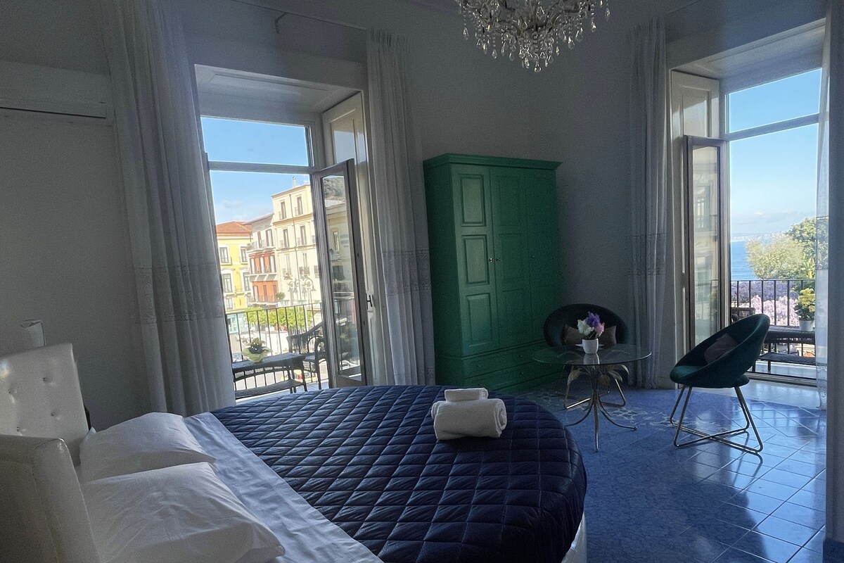Ein Schlafzimmer mit einem großen Bett, einem grünen Kleiderschrank, einem kleinen Tisch mit einer Vase und einem Stuhl.